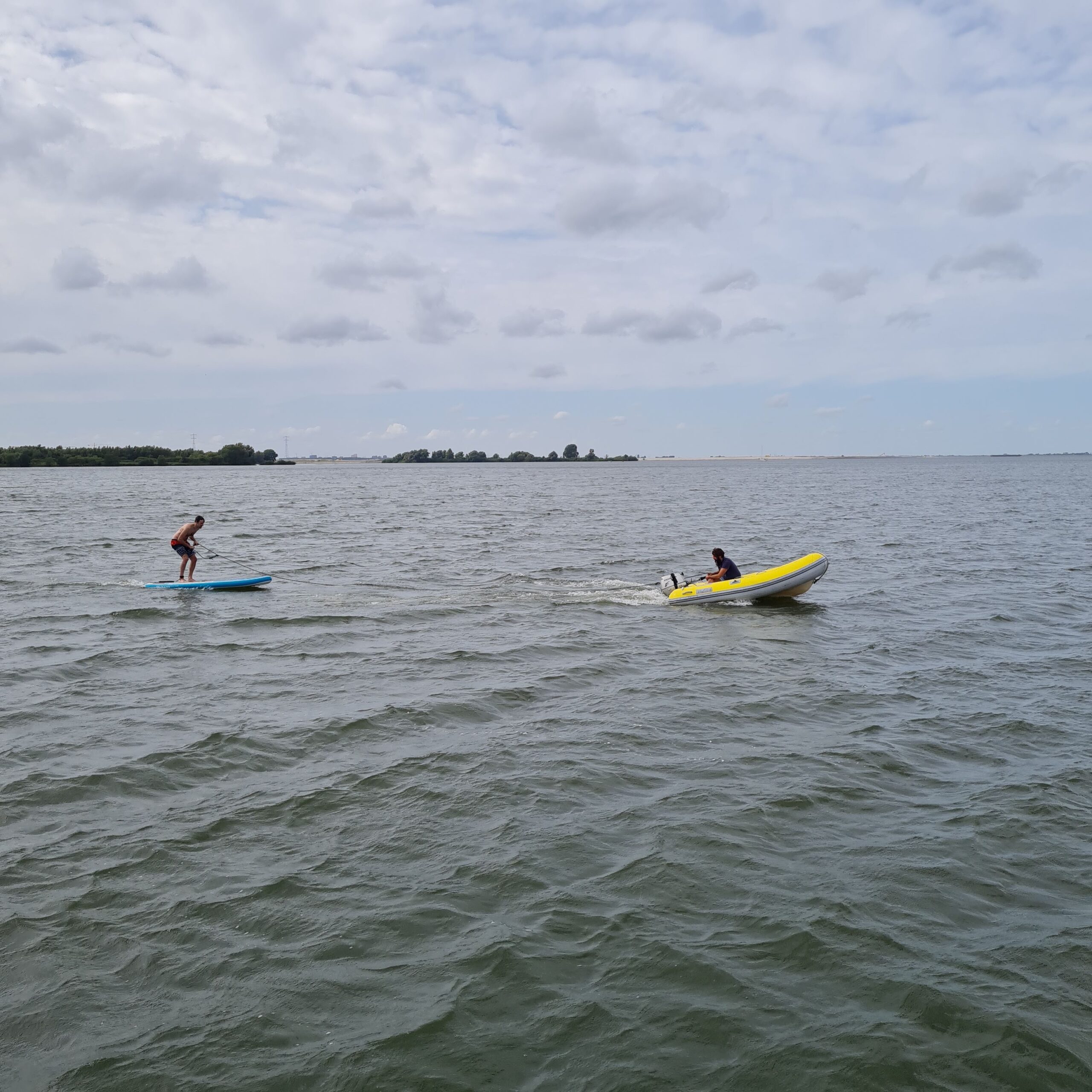 Paddleboarder and a dinghy sailor enjoying water sports on the choppy waters of Markermeer.