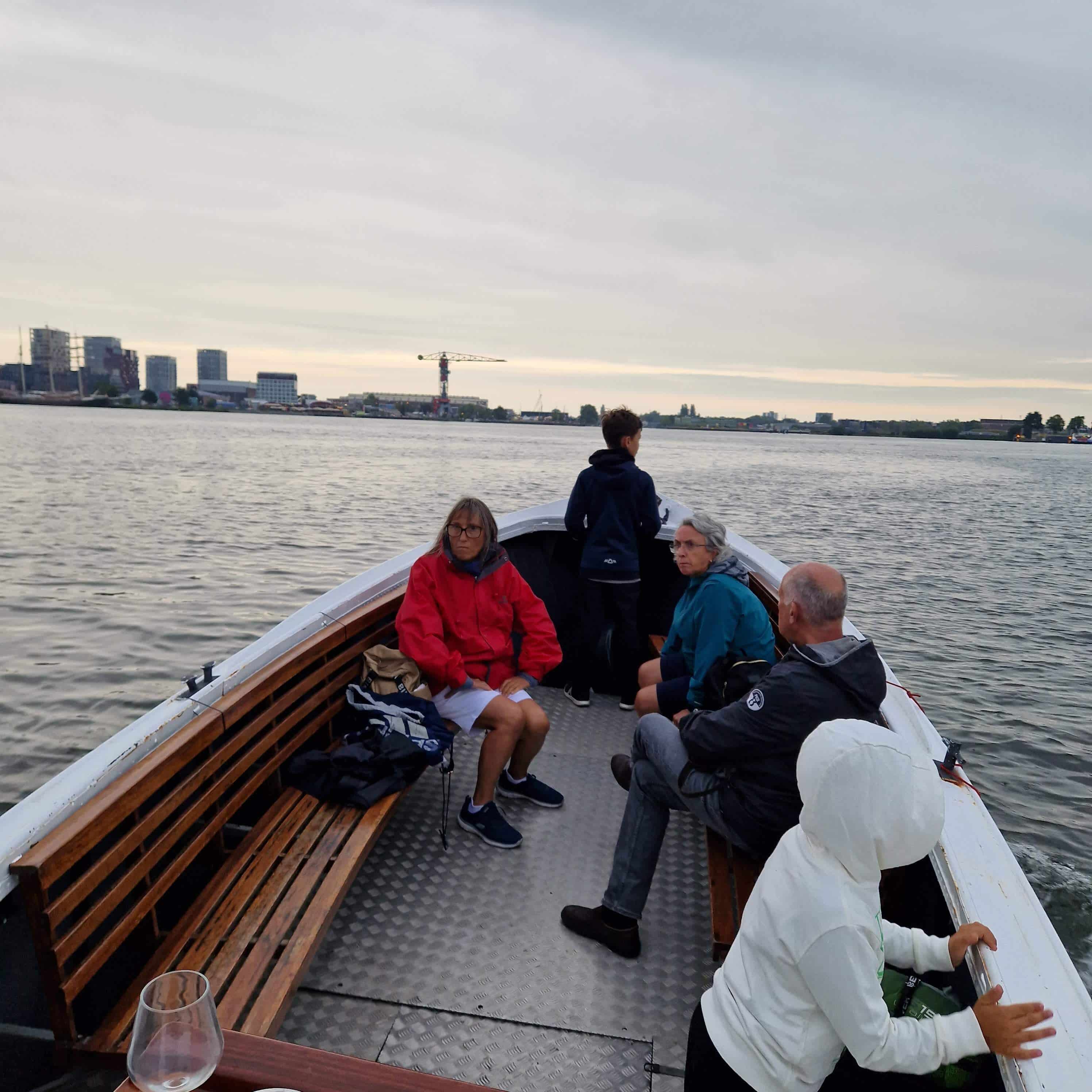 Passengers enjoying a serene evening boat tour on Amsterdam's expansive waterways with city skyline in the background