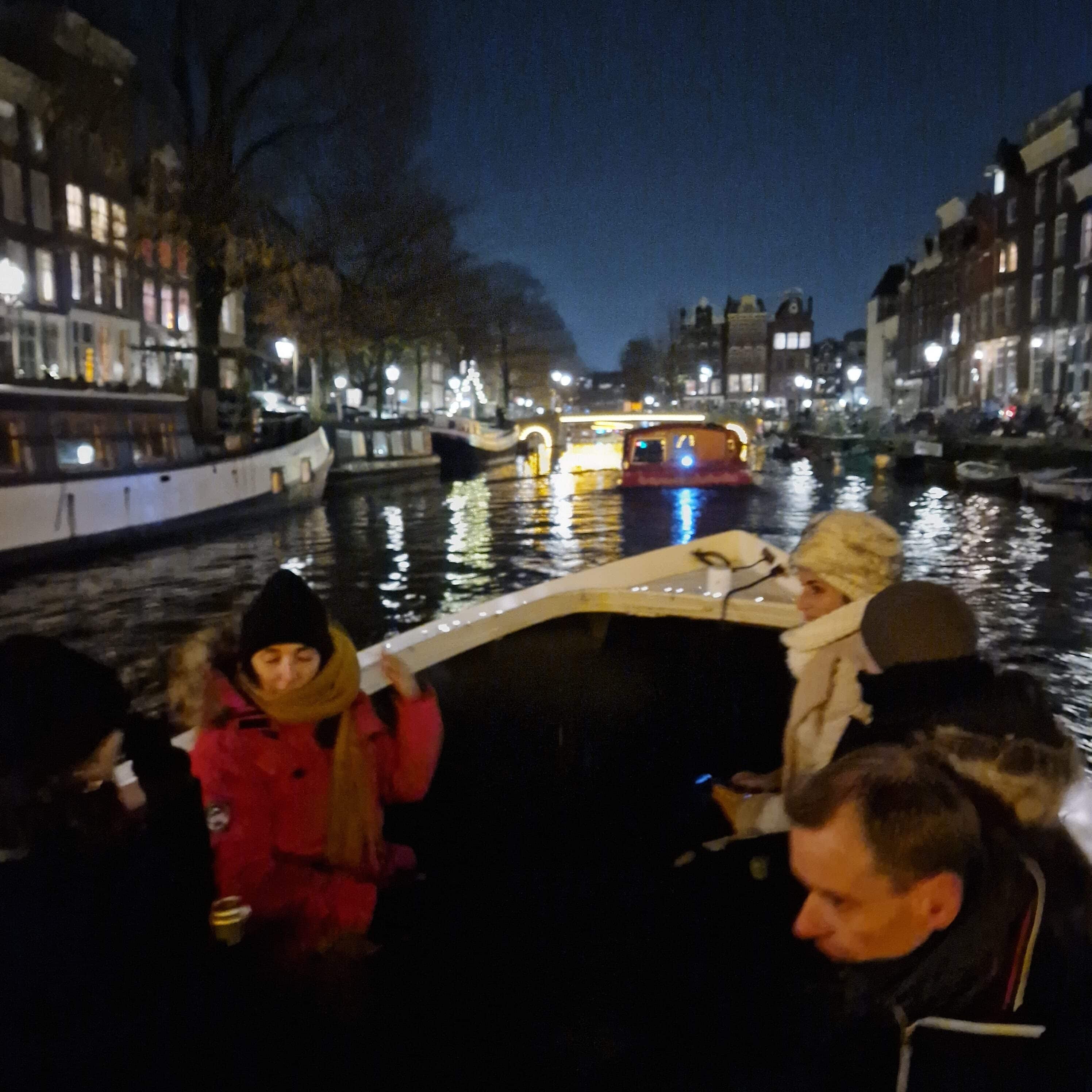 Sailing Saetta guests bundled up for an enchanting evening canal cruise in Amsterdam's illuminated waterways.